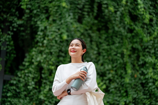 Smiling Woman with Sustainable Water Bottle Embracing Eco-Conscious Lifestyle in Verdant Setting