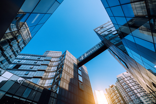 Low angle view of contemporary glass buildings converging under a clear blue sky.