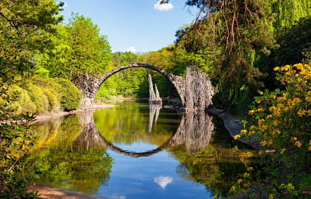 arch bridge (rakotzbrucke, devil’s bridge) in kromlau, germany, with reflections in calm water - forest pond landscaped water fotografías e imágenes de stock