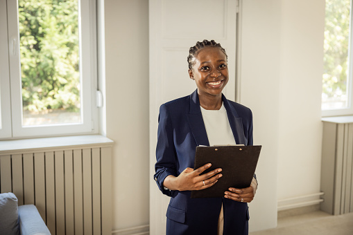 Smiling beautiful saleswoman holding digital tablet at empty new apartment.