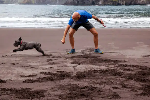 Man playing with his dog in the black sand beach of Seixal in Madeira Island north coast