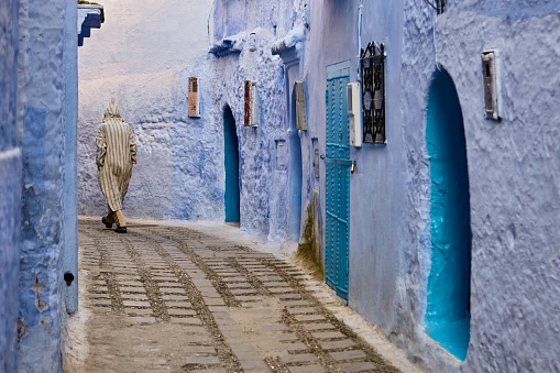 Blue street with man wearing djellaba in Chefchaouen, Morocco, North Africa.