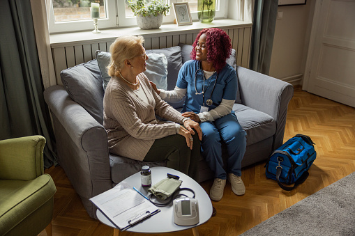Nurse visiting mature patient at home. She is talking to her about her condition and getting personal information's