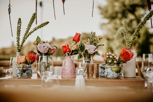 The roses and hydrangeas, arranged in ceramic vases and small glass jars, create a visually pleasing display when showcased on the wooden shelf.