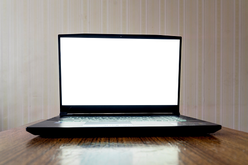 Empty white screen of laptop with mockup space located on old wooden surface of desktop at home or office room