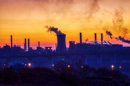 steel factory at sunset causing pollution smoke, global warming issue causing environmental issues ,view over the bridge