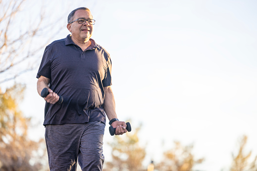 A Hispanic Senior working out outdoors at a park.
