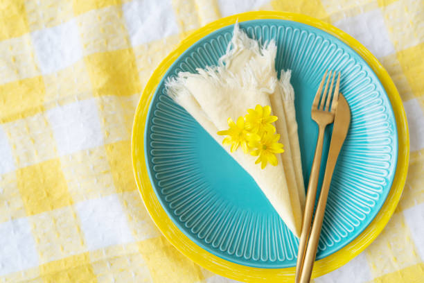 A bright blue plate with a yellow napkin, a wooden fork and fresh flowers on a checkered tablecloth. Table setting for the spring holiday