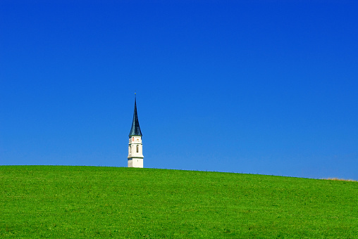 a church tower peeks out from behind a green hill, Upper Bavaria, Germany, Europe