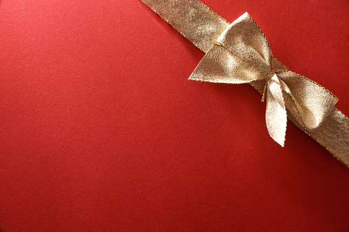 Gift wrap background detail with gold bow in one corner on textured red paper. Top view.