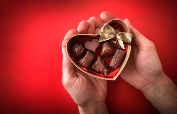 A bouquet made of assorted chocolates and fresh strawberries is being presented by a person in a stylish outfit. The vibrant colors and textures create an appealing display perfect for gifting.