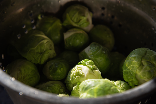 Fresh clean uncooked green Brussels sprouts in old metal colander with water drops. Selective focus. Real candid kitchen lifestyle background