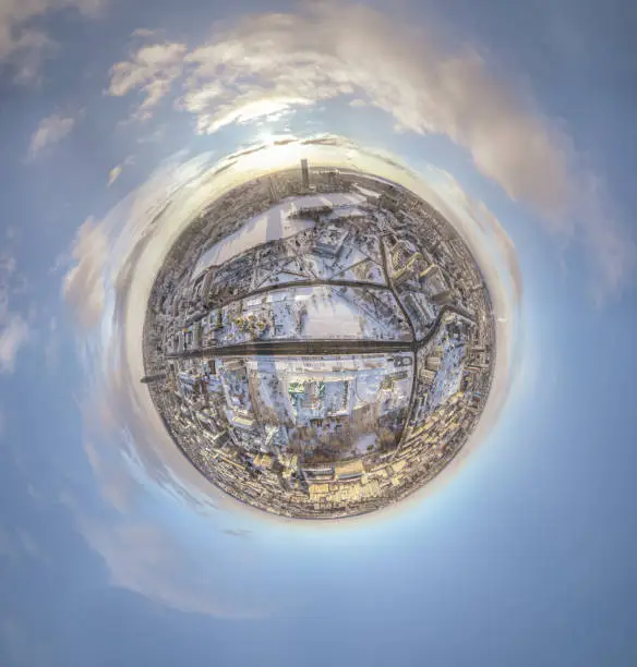 Photo of Aerial winter city view with crossroads and roads, houses, buildings, parks and bridges. Copter shot. Little planet sphere mode.