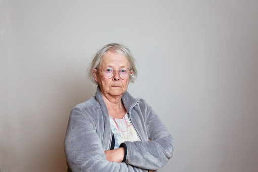 Portrait of a senior woman, 70 years old, with serious expression, wearing eyeglasses, a gray fleece jacket,armscrossed