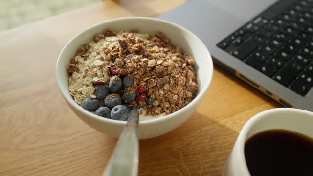 Lunchbreak with Healthy breakfast bowl with granola, blueberries, and a side of coffee and laptop.