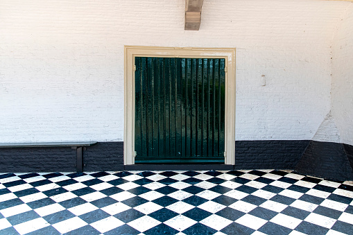 Zierikzee, The Netherlands-September 15, 2023; Abstract view of the white and black wall with green door of Gasthuiskerk church with checkered black and white stone floor