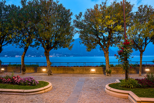 Lake Como, Italy. Lakefront walkway in Bellagio, old town on Lago di Como. Lombardy region. Summer trees and evening illumination during blue hour time the promenade.