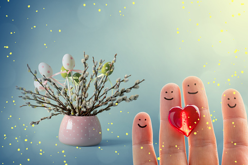 Pussy willow twigs with catkins and Easter eggs in a vase and happy finger family with a red heart. Defocused lights bokeh background, space for copy.