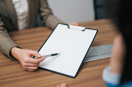 Hand of business woman holding pen and pointing to paper