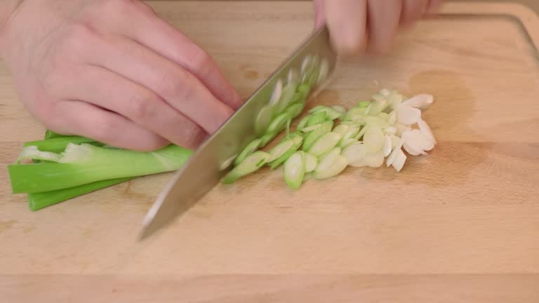 hand cutting spring onion on wooden chopping board