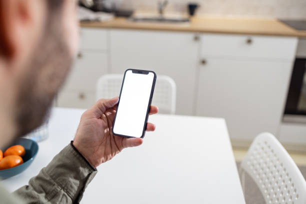 istock A male hand holding a smart phone with a blank screen. View from behind the shoulder: Internet surfing, text messaging, online shopping concept. 1978408046