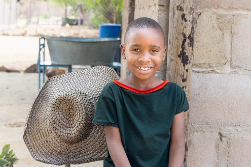 portrait of african child siting in the yard, village in Botswana, hat in the background