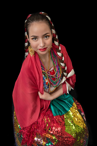 A mesmerizing glimpse into tradition: a Latin woman shines in a china poblana ensemble featuring an embroidered sequin skirt, red shawl, and braided bows.