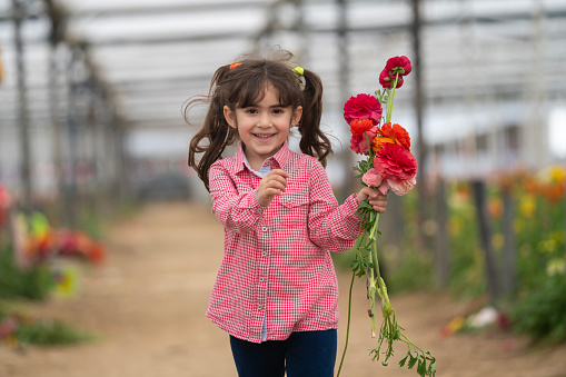 Photo of 5 years old girl holding a bouquet of flowers and running toward viewer. She is wearing a plaid shirt. Shot with a full frame mirrorless camera.