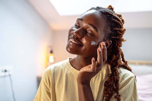 Young African American woman applying face cream and smiling