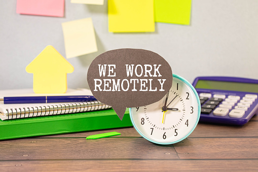 WORK REMOTELY text on a sticky with pen on the wooden background