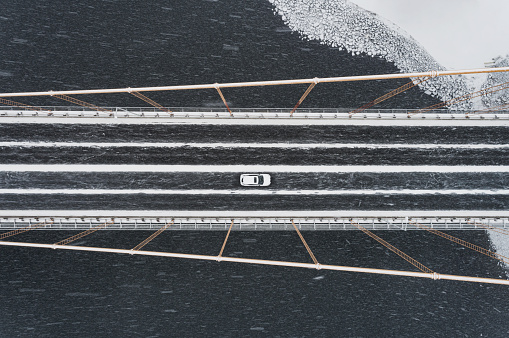 Aerial view of a single car crossing a suspension bridge during a snowstorm.