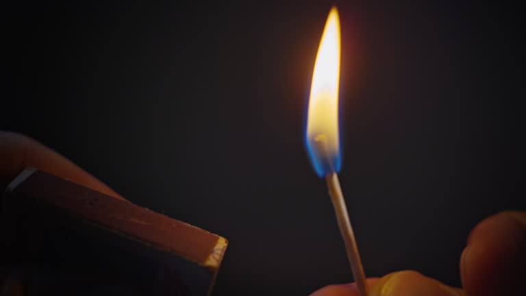 The match is lit on the box and burns in the dark. Taken in close-up.