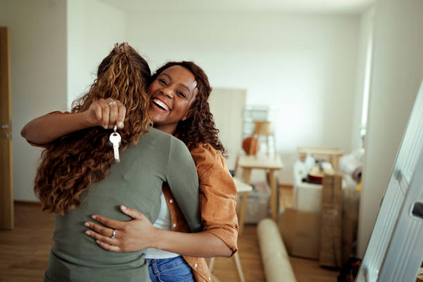 Happy for our new home! Lesbian couple hugging in their new apartment, one is holding house keys lesbian couple embracing stock pictures, royalty-free photos & images