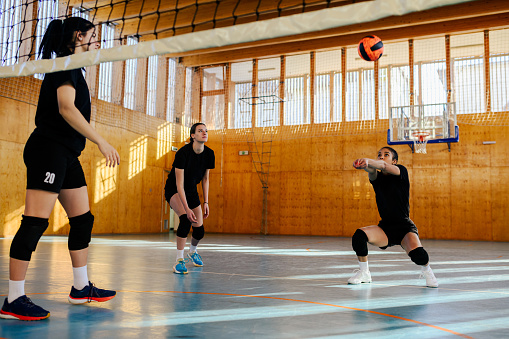 Multicultural female teenage volleyball players hitting and passing a ball on volleyball court during the training. A young interracial professional sportswomen practicing volleyball on indoor court.
