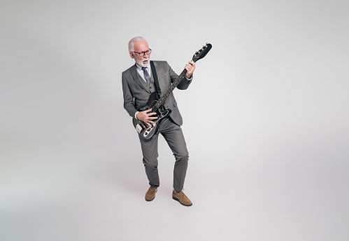 Full length of cheerful senior businessman singing and playing electric guitar on white background