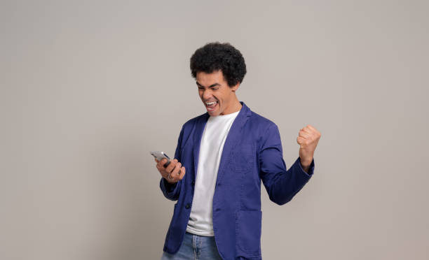istock Excited young man with mobile phone shouting ecstatically and playing air guitar on white background 1978689575