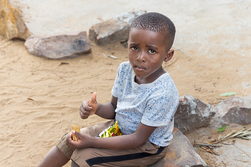 african child hanging in front of the house eating snacks and biscuits ,waiting for his mother
