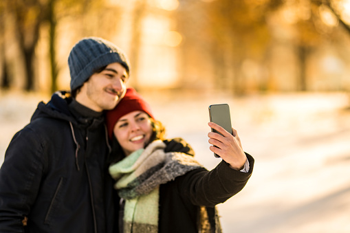 Beautiful young couple exploring and taking a selfie on a beautiful winter day in the city on sunset. Focus on foreground.
