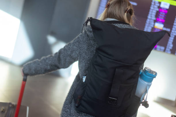 Unrecognizable woman is waiting for a flight, checking the departure time on the departure board