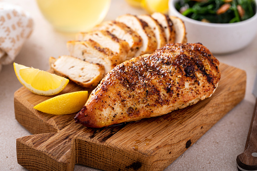 Grilled chicken breast whole and sliced on a cutting board with fresh lemon