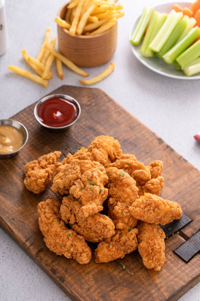istock Chicken nuggets or chicken strips on a board with dipping sauces, fries and celery 1978764049