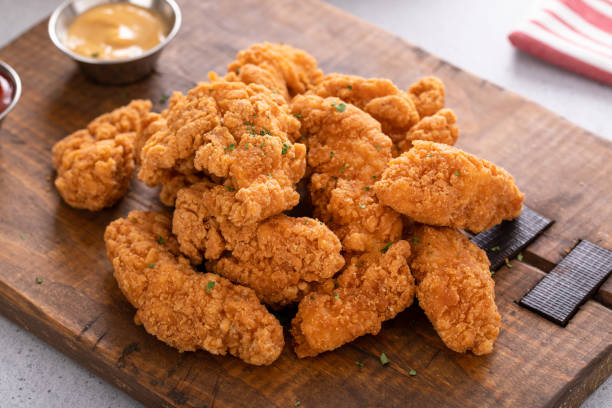 istock Chicken nuggets or chicken strips on a board with dipping sauces, fries and celery 1978764054