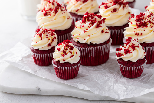 Red velvet cupcakes with cream cheese frosting and red velvet crumbs on a marble board