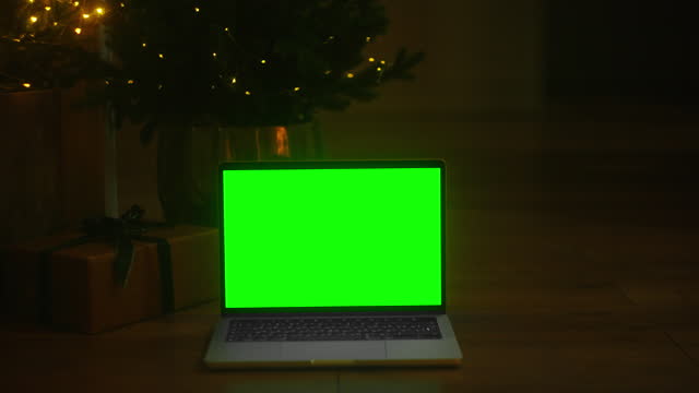 Unleash Your Creativity: Awe-Inspiring Video Footage of a Dark Room with a Green Screen Laptop and Christmas Tree