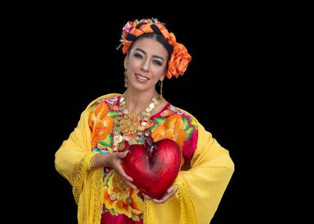 オアハカ州出身のメキシコ人ラテン系女性で、刺繍入りのスーツ、黄色のショール、取っ手の間にガラスのハートを挟んでいます - voguing ストックフォトと画像