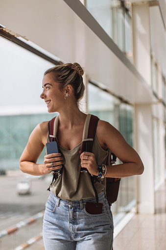 At the airport, a cheerful young woman carrying a backpack waits for her flight