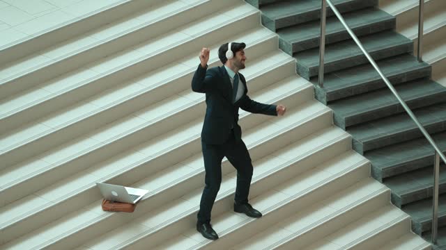 Business man standing at stair while moving to music from headphone. Exultant.