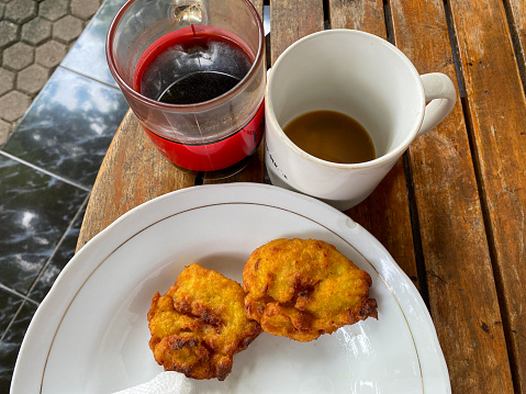 2 glasses of finished black coffee and 2 fried bananas on a white plate. Top view on stripes wooden table.