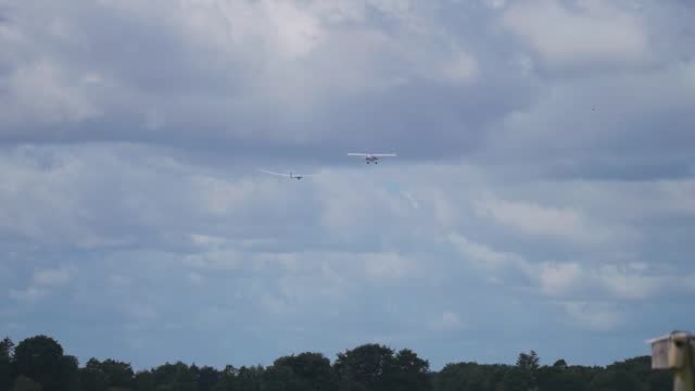 A light plane tows the glider high up into the stormy sky from the ground. More planes are lined up in the airport.