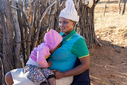 african mother holding her baby in the lap, outdoors kitchen in the background village in Botswana